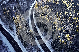 Aerial drone view of a curved winding road through the forest high up in the mountains in the winter with snow covered