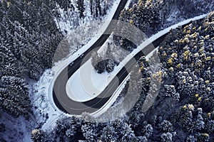 Aerial drone view of a curved winding road through the forest high up in the mountains in the winter with snow covered