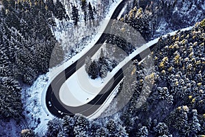 Aerial drone view of a curved winding road through the forest high up in the mountains in the winter with snow covered