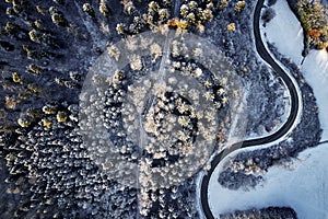 Aerial drone view of a curved winding road through the forest high up in the mountains in the winter with snow covered