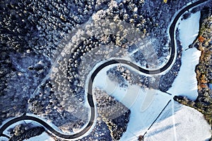 Aerial drone view of a curved winding road through the forest up in the mountains in the winter with snow covered trees