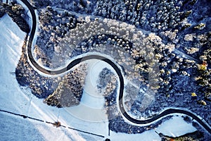 Aerial drone view of a curved winding road through the forest up in the mountains in the winter with snow covered trees