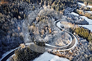 Aerial drone view of a curved winding road through the forest up in the mountains in the winter with snow covered trees