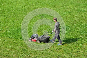 Aerial drone view of gardener mowing green grass lawn with motorized lawnmower in the garden. Landscaping service, gardening