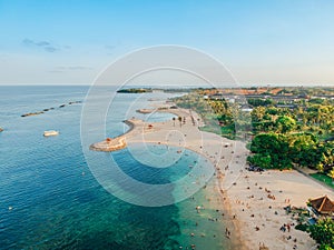 Aerial drone view of Holiday In Sanur Beach, Bali, Indonesia with ocean, boats, beach, villas, and people