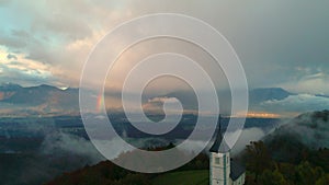 Aerial drone view of Jamnik, Slovenia. Rainbow, Alps and Church of St. Primoz