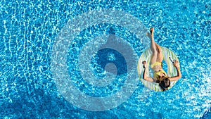 Aerial drone view of little girl in swimming pool from above, kid swims on inflatable ring donut , child has fun in blue water