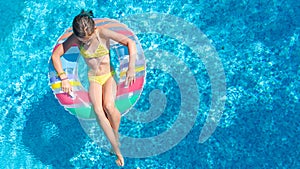 Aerial drone view of little girl in swimming pool from above, kid swims on inflatable ring donut , child has fun in blue water