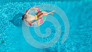 Aerial drone view of little girl in swimming pool from above, kid swims on inflatable ring donut , child has fun in blue water