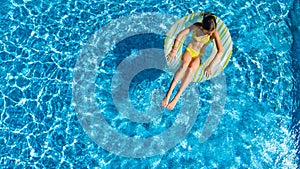 Aerial drone view of little girl in swimming pool from above, kid swims on inflatable ring donut , child has fun in blue water