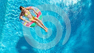 Aerial drone view of little girl in swimming pool from above, kid swims on inflatable ring donut , child has fun in blue water