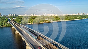 Aerial drone view of Metro railway bridge with train and Dnieper river from above, skyline of city of Kiev, Ukraine