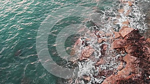 Aerial drone view of ocean waves hitting on rocks. Drone close-up view of rocky coast with big waves on a windy day