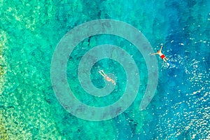 Aerial drone view of swimming men with red and gray swimming trunks in turquoise water. Ionian sea, Kefalonia Island, Greece