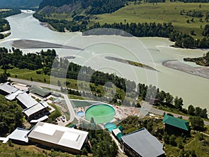 Aerial drone view on a tourist recreation center in the Altai mountains with hotel buildings and pools near green river on a warm