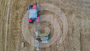Aerial drone view of tractor working in a wheat field creating straw bales, haystacks