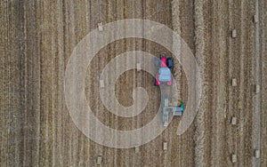 Aerial drone view of tractor working in a wheat field creating straw bales, haystacks