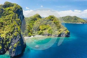 Aerial drone view of tropical beach with lonely boat on Entalula Island. Karst limestone formation mountain surrounded