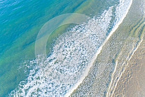 aerial drone view of the waves of a turquoise sea arriving at the shore of a beach in summertime