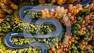 Aerial drone view of winding forest road in the middle of mountains. Colourful landscape with rural road, trees with yellow leaves