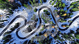 Aerial drone view winding mountain road between autumn trees and snow spruce forest. Serpentine snake road in Italian