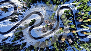 Aerial drone view winding mountain road between autumn trees and snow spruce forest. Serpentine snake road in Italian