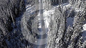 Aerial drone view of winter country road buried under snow. Pine tree forest road in the mountains