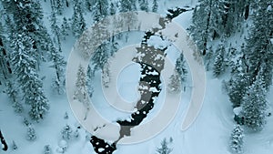 Aerial drone view on winter landscape with a river in a snowy mountain forest in a snowstorm. Winter Russia, Siberia