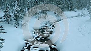 Aerial drone view on winter landscape with a river in a snowy mountain forest in a snowstorm. Winter Russia, Siberia