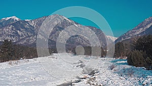 Aerial drone view of winter landscape of stream in gorge against the backdrop of the snow-capped mountains Arshan