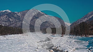 Aerial drone view of winter landscape of stream in gorge against the backdrop of the snow-capped mountains Arshan