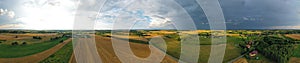 Aerial drone wide panoramic view on agricultural landscape with wheat field, village, meadows, forest and rain storm on horizon