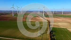 Aerial drone zoom out view of electric power pylon with wind turbines of a wink park in background