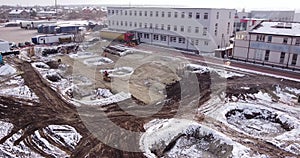 Aerial flight over the development of a site of new structures, where heavy machinery and construction workers work with