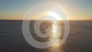 Aerial flight over the ocean at sunset. The drone flies into the distance against the backdrop of a sunny path. View of