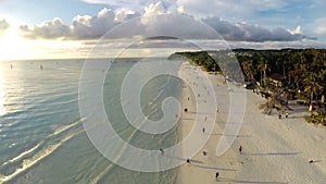 Aerial flight over sandy beach, waves and tourists