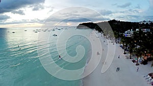 Aerial flight over sandy beach, waves and tourists