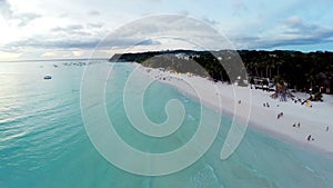 Aerial flight over sandy beach, waves and tourists