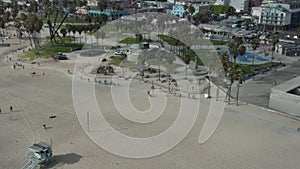 Aerial: flight towards Venice Beach skatepark and board walk with palm trees and bike lane, Sunny, Los Angeles