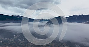 Aerial fly above clouds with blue white sky with mountains in the background.