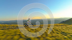 AERIAL: Flying along mountain biker pedalling his bicycle along the grassy trail