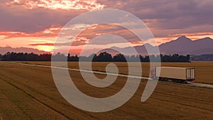 AERIAL: Flying along a truck hauling a container across countryside at sunrise.