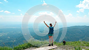 AERIAL: Flying around a girl standing atop of a mountain with outstretched arms.