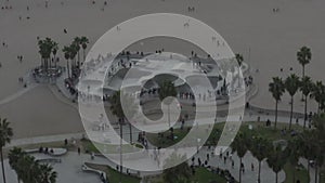 AERIAL: Flying away from Venice Beach Skatepark with Visitors and Palm Trees, Sunset in Los Angeles
