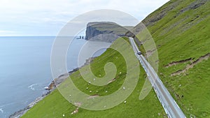 AERIAL: Flying behind a car cruising along a coastal road in Faroe Islands.