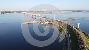 Aerial flying with locomotive pulls into a bridge over a river at sunset