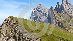 AERIAL: Flying next to young woman hiking up the grassy hill with her puppy.