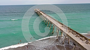 aerial footage of the blue ocean water along the coastline at Johnnie Mercer\'s Fishing Pier with people on the sand