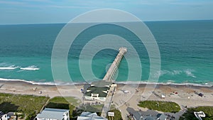 aerial footage of the blue ocean water along the coastline at Johnnie Mercer\'s Fishing Pier with people on the sand