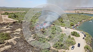 Aerial footage of a brush fire along the silky green waters of the Colorado River surrounded by dry brush and lush green trees